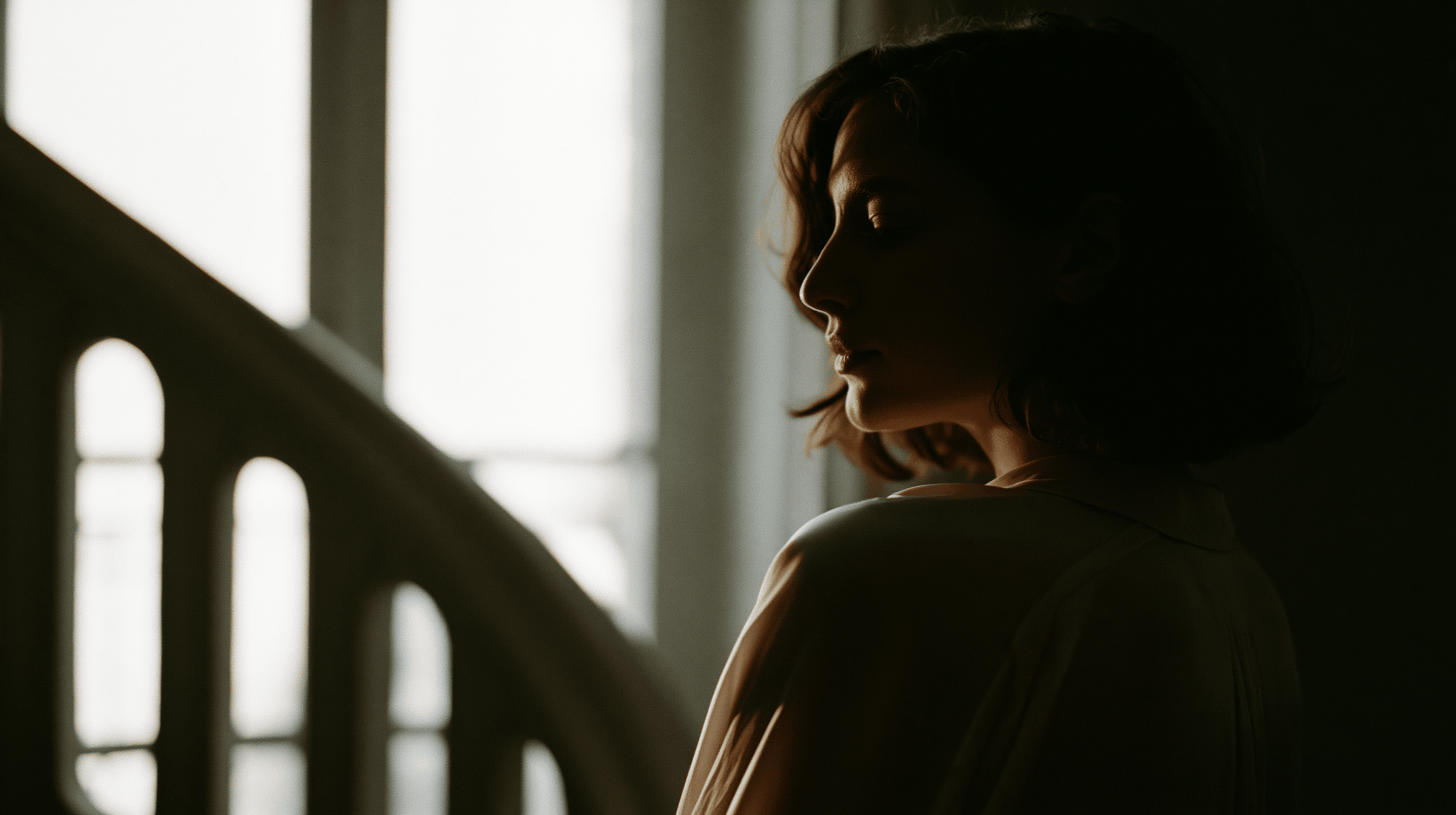 A woman in profile at a bright window, poised in quiet light